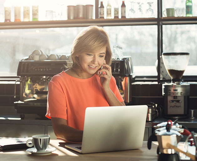 A shop keeper on the phone with the bank while working on a laptop