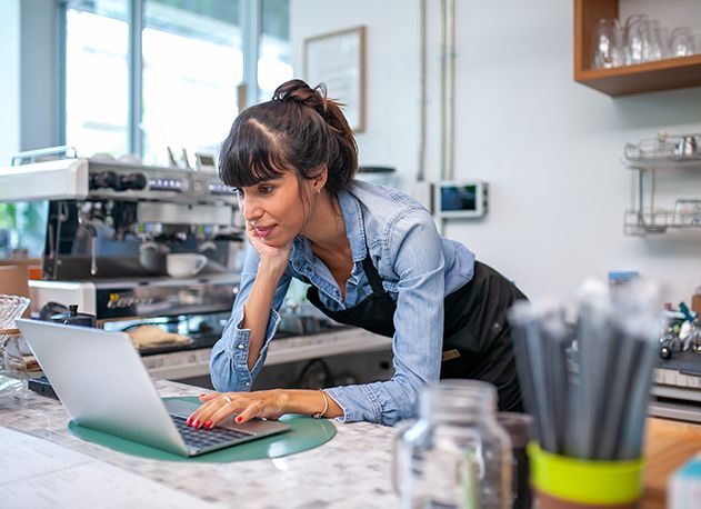 A woman behind a coffeeshop counter looking at a laptop